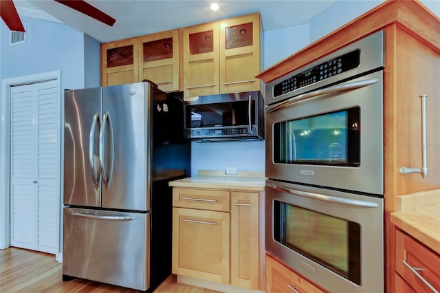 kitchen with light countertops, glass insert cabinets, light wood-style flooring, stainless steel appliances, and visible vents