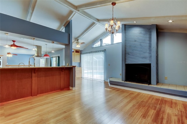 unfurnished living room featuring a large fireplace, light wood-style flooring, high vaulted ceiling, beamed ceiling, and ceiling fan with notable chandelier