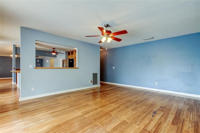 unfurnished living room with a ceiling fan, visible vents, baseboards, and wood finished floors