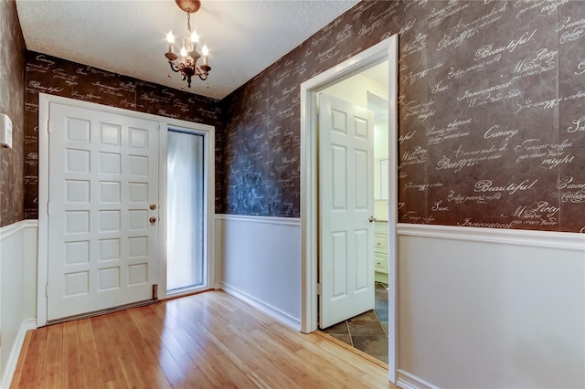 foyer entrance featuring a wainscoted wall, a textured ceiling, wallpapered walls, wood finished floors, and a notable chandelier