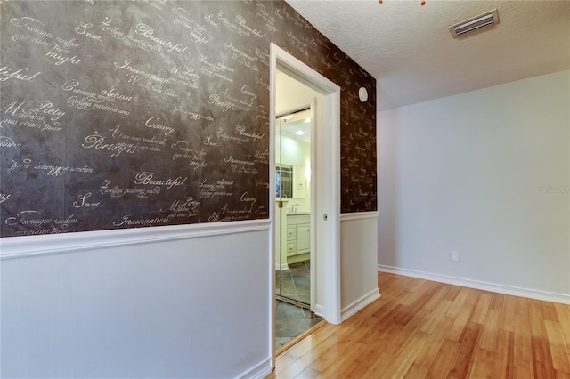 hall featuring hardwood / wood-style floors, a textured ceiling, wallpapered walls, visible vents, and wainscoting