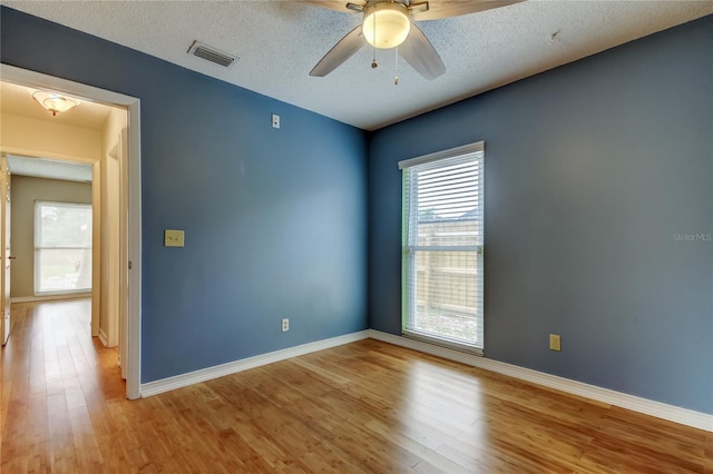 empty room with baseboards, a textured ceiling, visible vents, and light wood finished floors