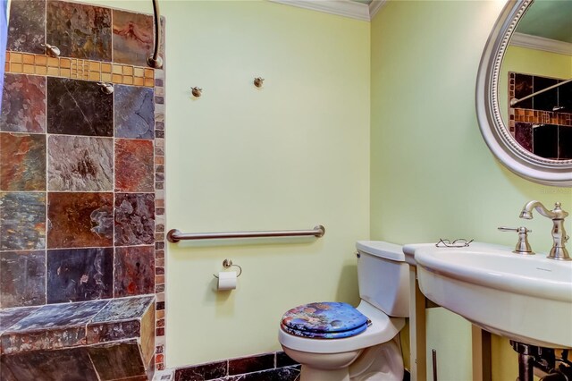 bathroom featuring toilet, a sink, crown molding, and a tile shower