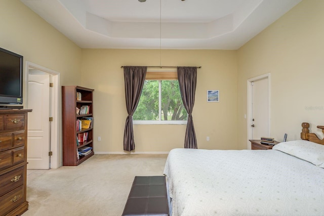 bedroom featuring baseboards, a raised ceiling, and light carpet