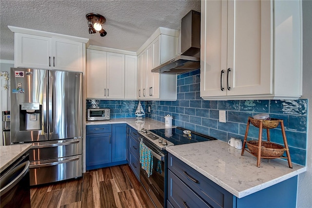kitchen featuring dark wood finished floors, blue cabinets, wall chimney exhaust hood, and appliances with stainless steel finishes
