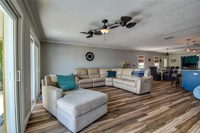 living area featuring crown molding, a textured ceiling, dark wood-style floors, visible vents, and a ceiling fan