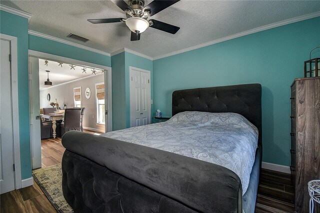 bedroom featuring ornamental molding, baseboards, a textured ceiling, visible vents, and wood finished floors