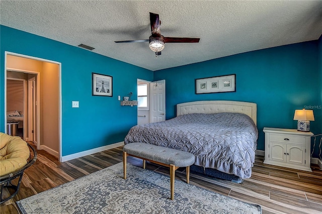 bedroom featuring baseboards, a textured ceiling, visible vents, a ceiling fan, and wood finished floors