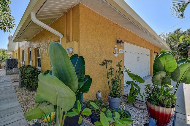 view of home's exterior with stucco siding, a garage, central air condition unit, and fence