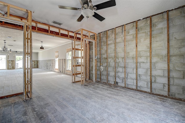 interior space featuring concrete block wall, a ceiling fan, crown molding, and visible vents