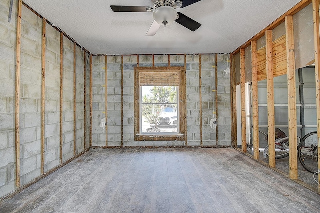 unfurnished room with concrete block wall, a ceiling fan, and a textured ceiling