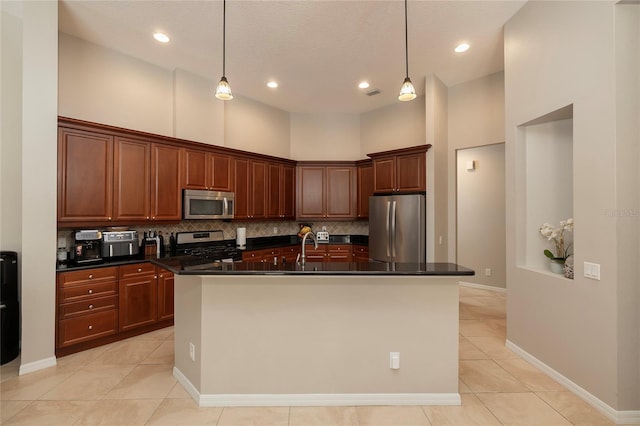 kitchen featuring a kitchen island with sink, dark countertops, backsplash, and appliances with stainless steel finishes
