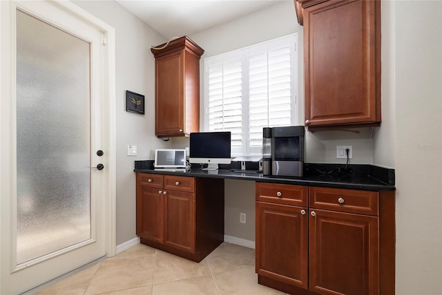 kitchen with baseboards, built in desk, brown cabinetry, and light tile patterned floors