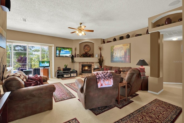 living area with carpet flooring, a warm lit fireplace, a textured ceiling, visible vents, and ceiling fan