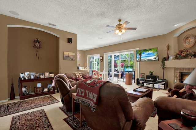 carpeted living room featuring a textured ceiling, visible vents, a fireplace, ceiling fan, and arched walkways