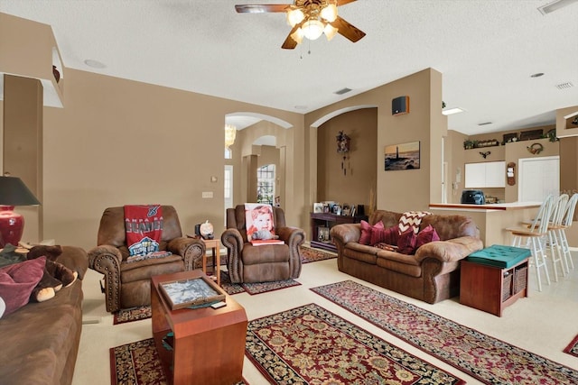 carpeted living area with a ceiling fan, visible vents, arched walkways, and a textured ceiling