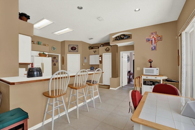 kitchen with light tile patterned flooring, a kitchen breakfast bar, a peninsula, white appliances, and visible vents