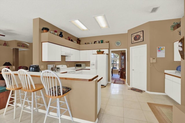 kitchen featuring a kitchen bar, white appliances, light tile patterned floors, under cabinet range hood, and a peninsula