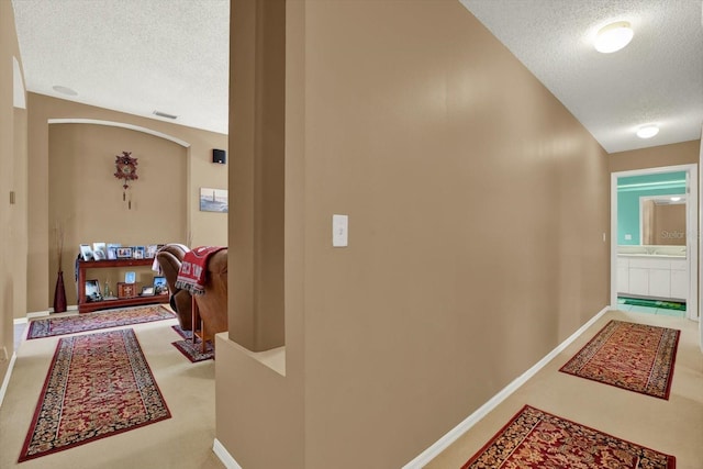 corridor featuring baseboards, arched walkways, carpet flooring, and a textured ceiling