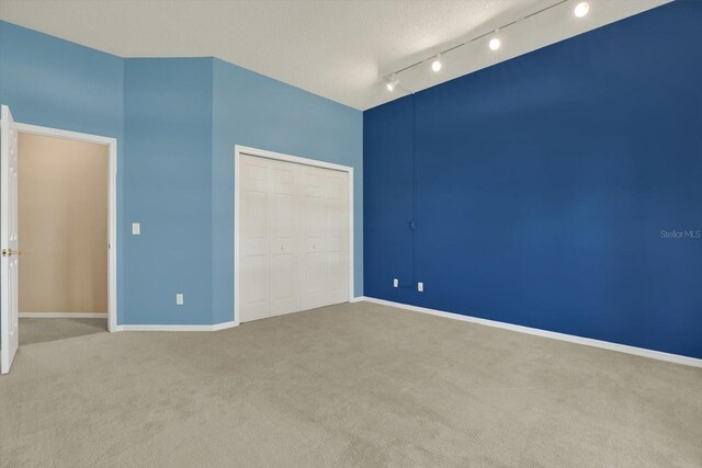 unfurnished bedroom with carpet flooring, rail lighting, baseboards, and a closet