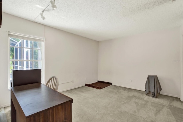 unfurnished office featuring light carpet, baseboards, rail lighting, and a textured ceiling