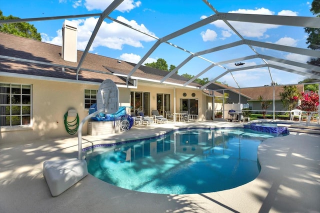 view of pool featuring glass enclosure, a pool with connected hot tub, and a patio area