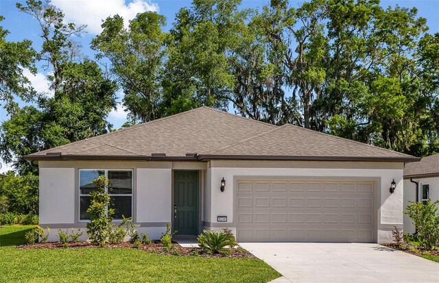 ranch-style house with a front lawn, roof with shingles, stucco siding, an attached garage, and driveway