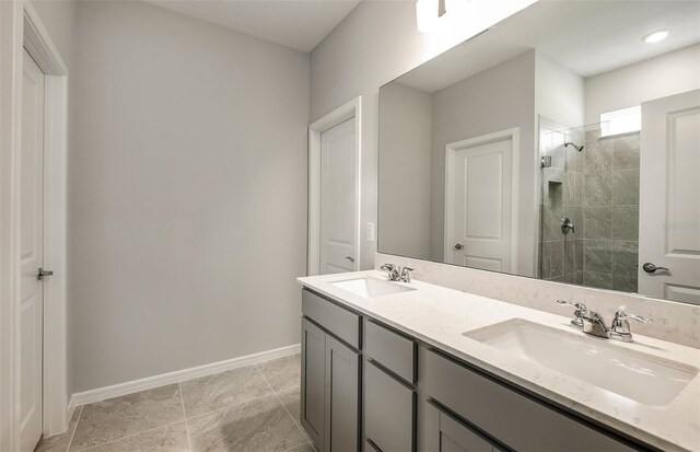 bathroom with double vanity, a sink, baseboards, and tiled shower