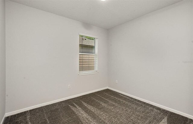 empty room featuring baseboards and dark colored carpet