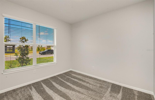 empty room with baseboards and dark colored carpet