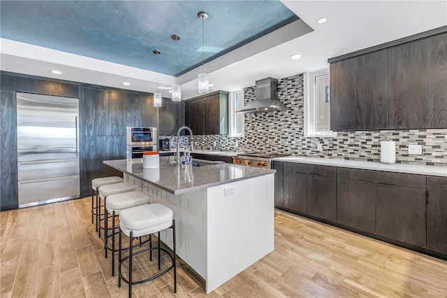 19816 Gulf Blvd Unit 201, Indian Shores, FL 33785 - kitchen with light wood-style flooring, a tray ceiling, a breakfast bar, a sink, and wall chimney exhaust hood