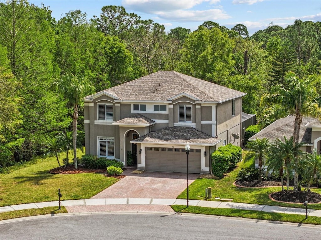 traditional home featuring a front lawn, driveway, stucco siding, and a view of trees