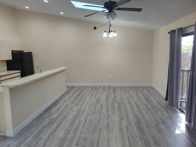 interior space featuring a skylight, a textured ceiling, baseboards, light wood-style floors, and ceiling fan