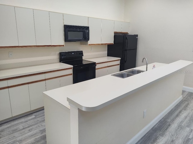 kitchen with light countertops, a sink, black appliances, and light wood-style flooring