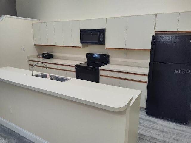 kitchen with light countertops, a sink, black appliances, and light wood-style flooring