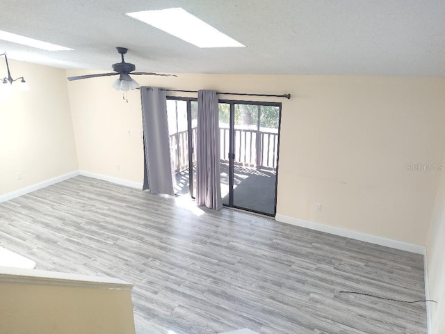 empty room with a ceiling fan, wood finished floors, a skylight, a textured ceiling, and baseboards