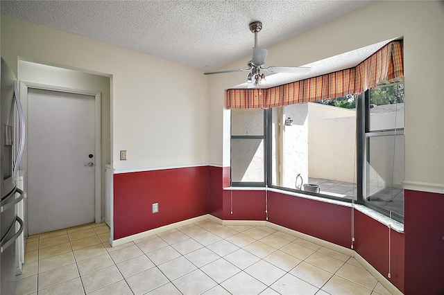unfurnished dining area featuring baseboards, a textured ceiling, ceiling fan, and light tile patterned floors