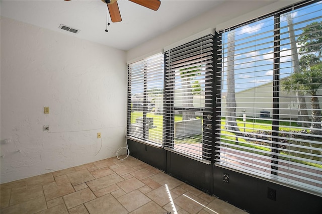 unfurnished room featuring visible vents, a ceiling fan, stone finish flooring, and a textured wall