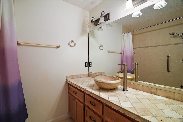 full bath with a textured ceiling, a tile shower, and vanity