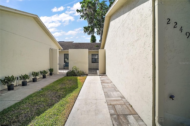 entrance to property featuring a gate, roof with shingles, and stucco siding