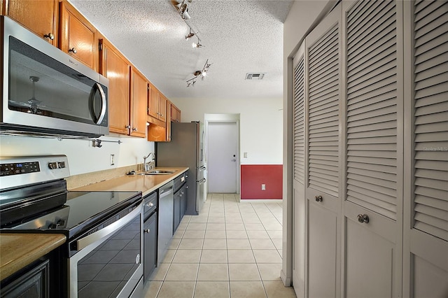 kitchen featuring brown cabinetry, visible vents, rail lighting, a sink, and stainless steel appliances