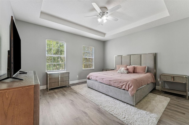 bedroom featuring a raised ceiling, wood finished floors, baseboards, and ceiling fan