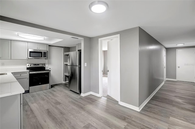 kitchen with gray cabinetry, light countertops, light wood-style flooring, and appliances with stainless steel finishes