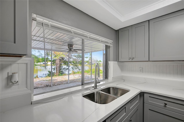 kitchen featuring gray cabinets, light stone countertops, a sink, and a ceiling fan