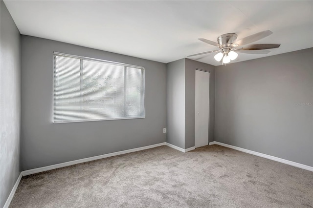 carpeted empty room with a ceiling fan and baseboards