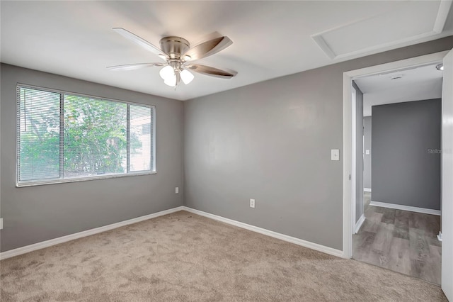 carpeted spare room featuring baseboards, ceiling fan, and attic access