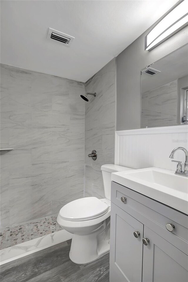 full bath with toilet, tiled shower, vanity, wainscoting, and visible vents