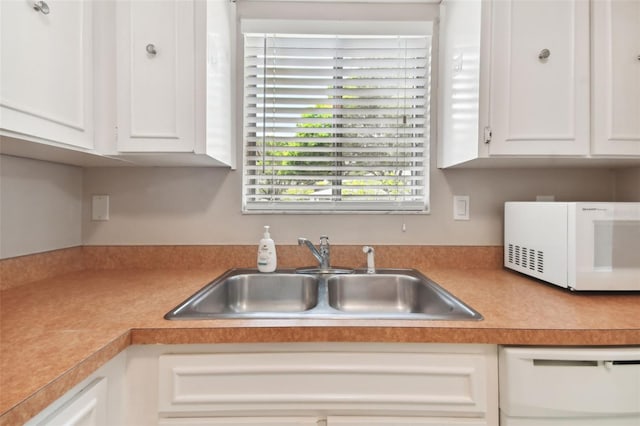 kitchen featuring white appliances, white cabinets, light countertops, and a sink