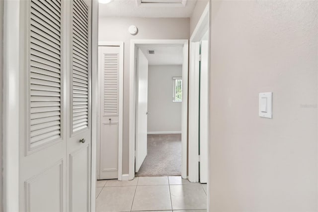 hallway with a textured ceiling, visible vents, baseboards, light carpet, and light tile patterned floors