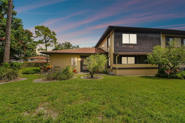 back of house at dusk featuring stucco siding and a yard